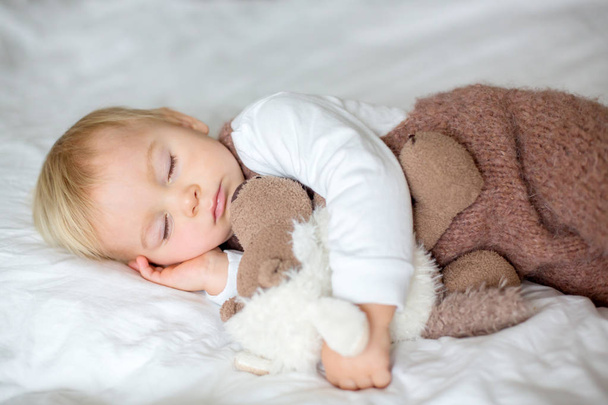 Sweet baby boy in cute overall, sleeping in bed with teddy bear stuffed toys, winter landscape behind him - Fotoğraf, Görsel