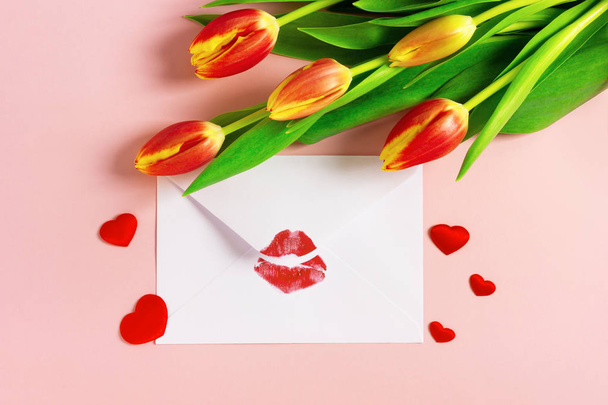 Fondo del día de San Valentín. Concepto de carta de amor. Sobre blanco con lápiz labial rojo beso, corazones rojos y ramo de tulipanes en pastel rosa
. - Foto, imagen
