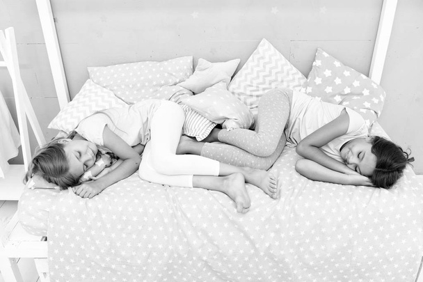 Good night and sweet dreams. Girls fall asleep after pajamas party in bedroom. Girls have healthy sleep. Children relax on bed. Sleepy kids in pajamas having rest on comfortable bed. Happy childhood - Foto, Bild