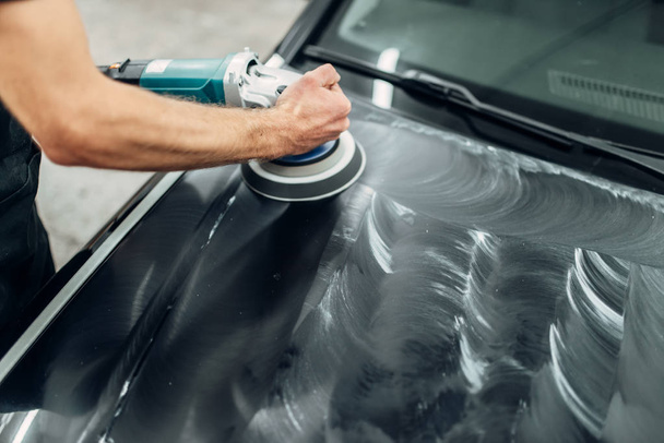 Male person with polishing machine cleans car hood. Auto detailing on carwash service, restore the paint of vehicle - Fotoğraf, Görsel