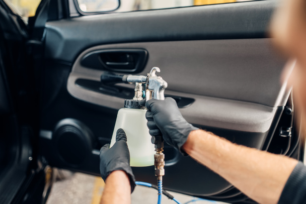 Carwash service, male worker in gloves using special spray. Professional dry cleaning of car door trim, vehicle interior hygiene - Foto, afbeelding