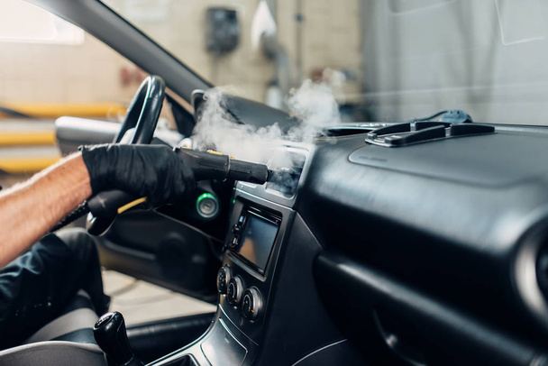 Автомойка, мужчина в перчатках удаляет пыль и грязь с помощью пароочистителя. Профессиональная химчистка салона автомобиля
 - Фото, изображение