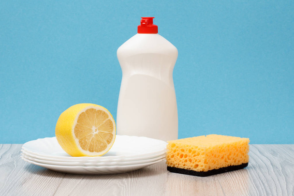 Plastic bottle of dishwashing liquid, clean plates, lemon and sponge on blue background. Washing and cleaning concept. - Photo, Image