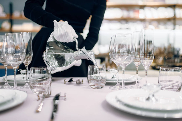 Camarera en guantes vierte bebidas en vasos, mesa puesta. Servicio de servir, decoración de la cena festiva
 - Foto, Imagen