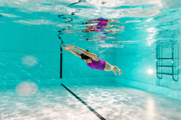  mujer buceando bajo el agua en traje de baño rosa en agua azul de la piscina
 - Foto, Imagen