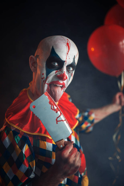 Eng bloedige clown likt het mes mes. Man met make-up in halloween kostuum, gekke maniak houdt menselijke hand - Foto, afbeelding