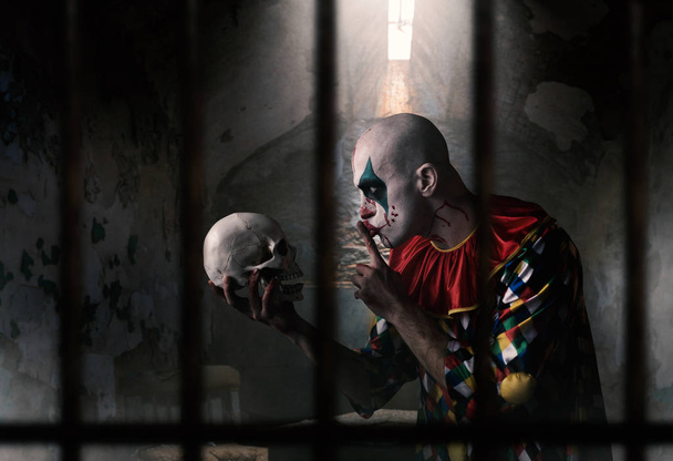 Божевільний клоун з людським черепом показує тихий знак, жахливий секрет. Чоловік з макіяжем в карнавальному костюмі, божевільний маніяк
 - Фото, зображення