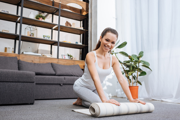 selective focus of smiling woman rolling fitness mat for practicing yoga at home - Φωτογραφία, εικόνα