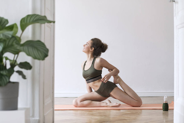 Young woman in green sportswear practicing yoga at home  - Фото, зображення