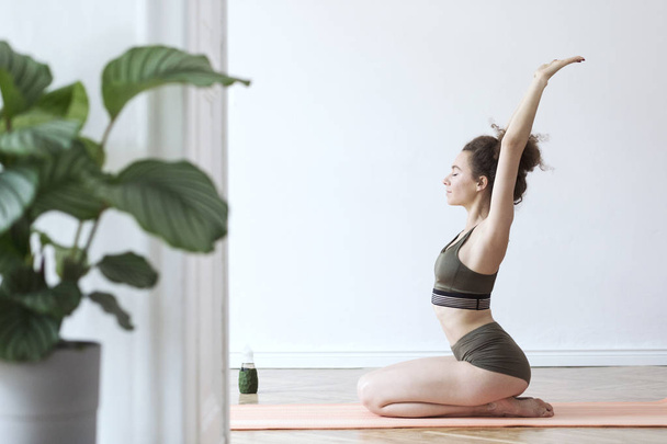 junge Frau in grüner Sportbekleidung praktiziert Yoga zu Hause  - Foto, Bild