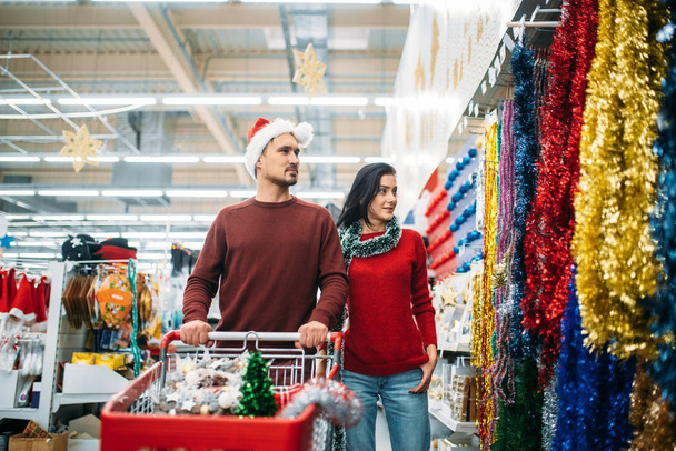 Young couple in the department of holiday decorations in supermarket, family tradition. December shopping - Photo, image