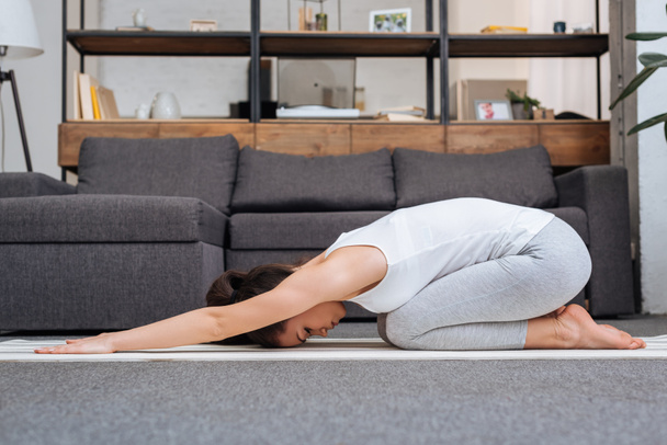 woman practicing balasana at home in living room - Foto, afbeelding