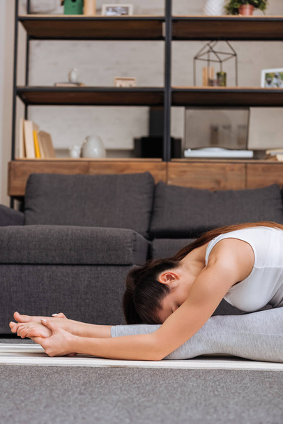 donna che pratica seduta piega in avanti posa sul tappeto fitness a casa in soggiorno
 - Foto, immagini