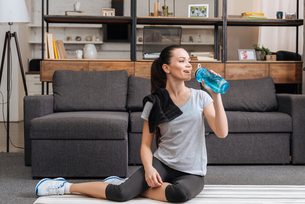 beautiful athletic sportswoman drinking water from sport bottle at home - Foto, imagen