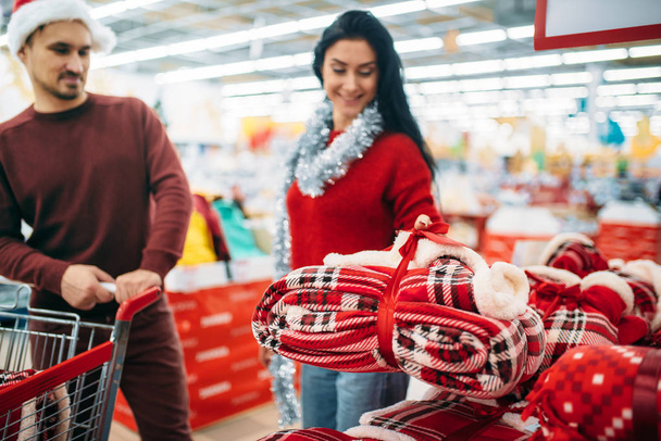 Пара покупает рождественский костюм в супермаркете, семейные традиции. Декабрь покупки новогодних товаров и украшений
 - Фото, изображение