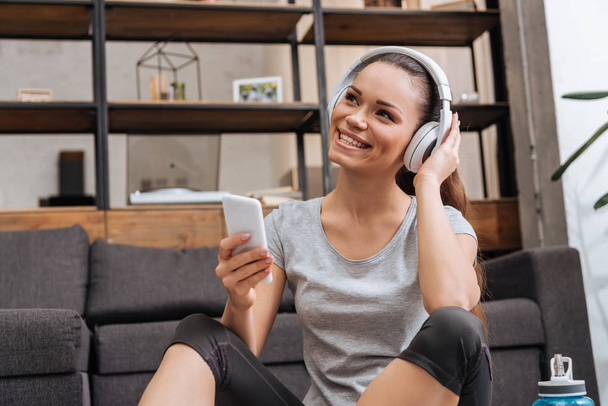 beautiful smiling woman in headphones using smartphone at home - Fotó, kép
