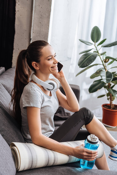 smiling sportswoman with headphones talking on smartphone at home - Photo, Image