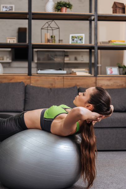 selective focus of focused sportswoman exercising with fitness ball at home - Foto, afbeelding