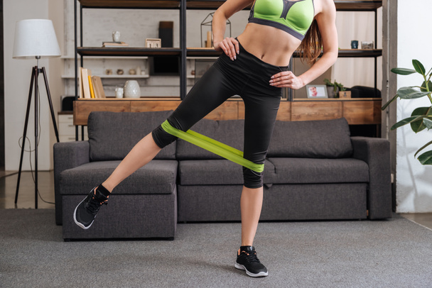 partial view of sportswoman training with resistance band at home in living room - Foto, imagen