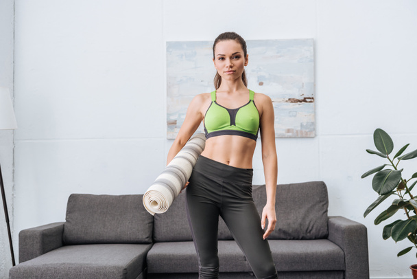 beautiful athletic sportswoman with fitness mat looking at camera at home - Photo, Image