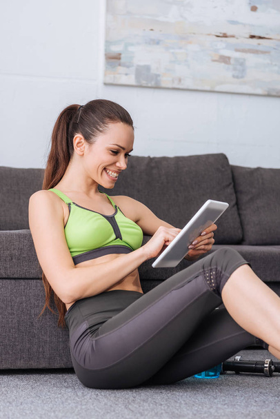 smiling sportswoman sitting and using digital tablet at home - Photo, Image