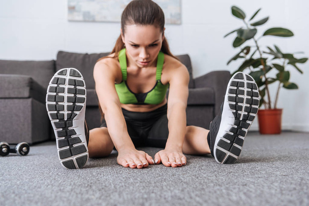 selective focus of sportswoman sitting and doing stretching exercise at home - Fotoğraf, Görsel