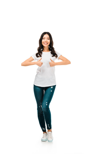 full length view of happy brunette girl showing thumbs up and smiling at camera isolated on white  - Photo, Image