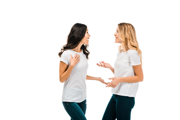 Gelukkig jonge vrouwen in witte t-shirts praten en kijken elkaar geïsoleerd op wit - Foto, afbeelding