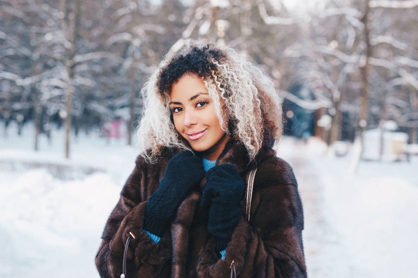 Outdoor close up portrait of young beautiful fashionable woman with afro hair , wearing fur coat in winter park. Winter fashion, Christmas holidays concept. - Photo, image
