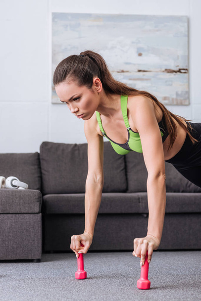focused sportswoman doing push ups with dumbbells at home - Valokuva, kuva