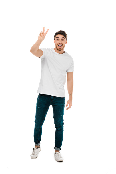 full length view of happy young man showing victory sign and smiling at camera isolated on white - Foto, imagen