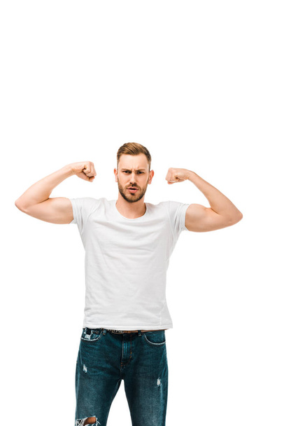 handsome bearded young man showing biceps and looking at camera isolated on white  - 写真・画像