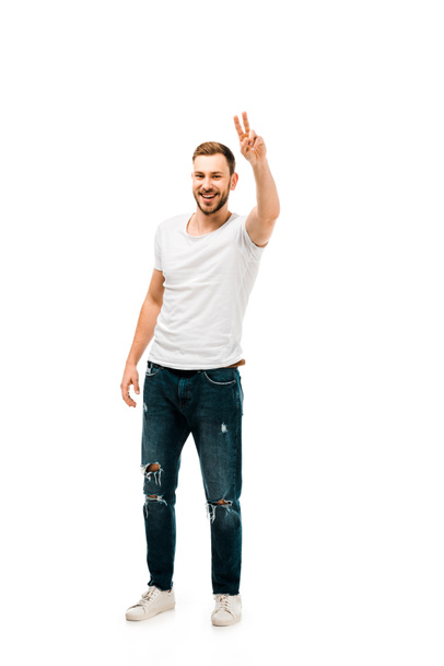Вид в полный рост на красивого счастливого человека, показывающего знак победы и смотрящего на камеру, изолированную от белого
 - Фото, изображение