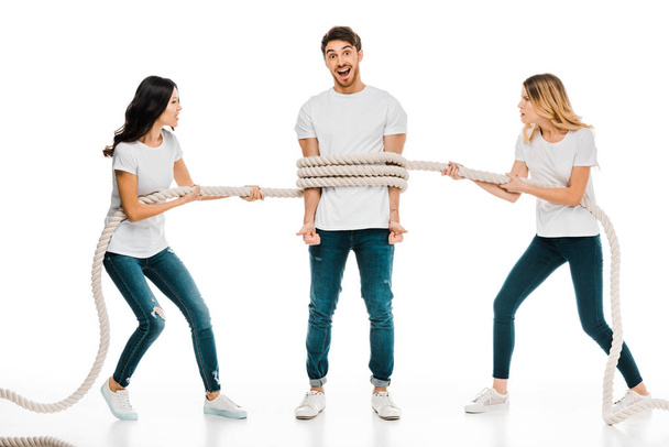emotionele jonge vrouwen houden van touw rond de jonge man die lacht op camera geïsoleerd op wit  - Foto, afbeelding