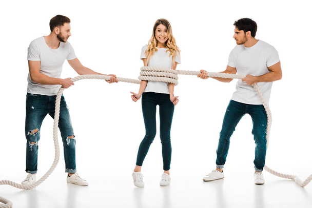young men holding rope wrapped around smiling young woman showing thumbs up and looking at camera isolated on white - Foto, Imagem