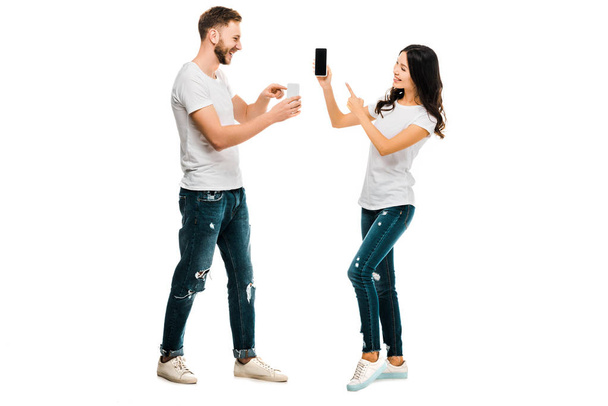 щаслива молода пара показує один одному смартфони ізольовані на білому
 - Фото, зображення