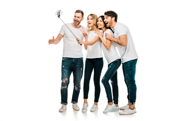 happy young male and female friends standing together and taking selfie with smartphone and selfie stick isolated on white - Fotografie, Obrázek