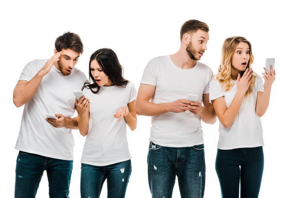 шокированные молодые пары, держащие в руках смартфоны, изолированные на белом
 - Фото, изображение