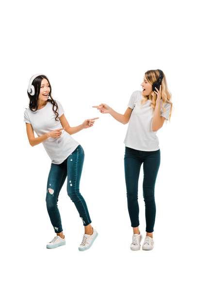 красиві щасливі дівчата в навушниках танцюють і вказують пальцями ізольовані на білому
 - Фото, зображення