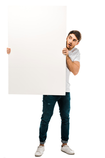 jovem assustado segurando banner em branco e olhando para o espaço de cópia isolado no branco
 - Foto, Imagem