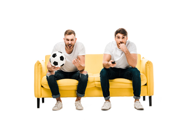 emotional young men with soccer ball sitting on couch and watching sports match isolated on white - 写真・画像