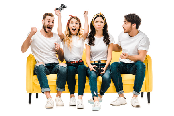 emotional young friends sitting on couch and playing with joysticks isolated on white  - Foto, Bild