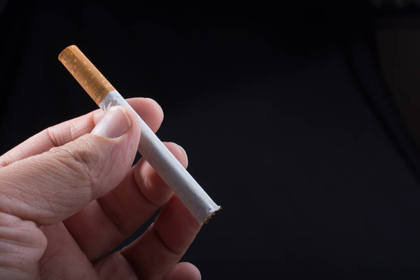 Рука тримає сигарету на чорному тлі
 - Фото, зображення