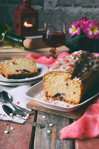 Dried fruit cake with raisins, apricots, cherry and glass of red wine, bottle and flower rustic wooden background. Valentines day still life. Sliced freshly baked fruitcake. Copy space for text. - Photo, Image