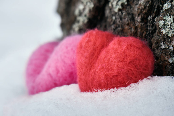 Deux coeurs rouges et roses lainés couchés sur la neige blanche près d'un tronc d'arbre à l'extérieur en hiver. Amour, santé, concept d'amitié. Vue latérale
. - Photo, image