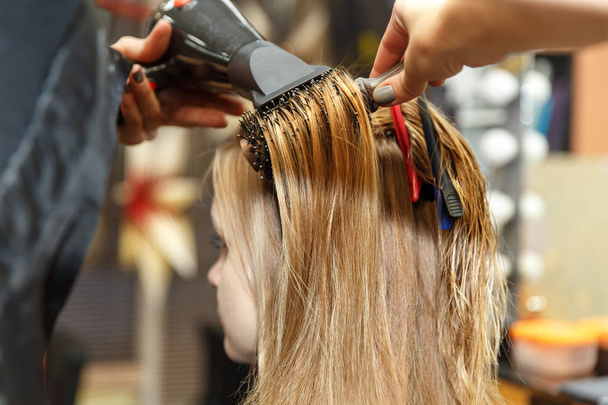Επαγγελματία κομμωτή βαφή μαλλιών του πελάτη της στο σαλόνι. Haircutter ξηρά μαλλιά με στεγνωτήρα μαλλιών. Επιλεκτική εστίαση. - Φωτογραφία, εικόνα