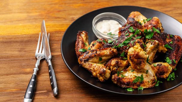 Baked chicken wings in Mexican with curry seasoning and parsley on a black plate, on a wooden background. side view, copy space, top view - Photo, Image