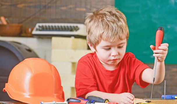 Closeup blond kid in workshop. Boy binding screws to wooden board. Concentrated child learning new skills - Φωτογραφία, εικόνα
