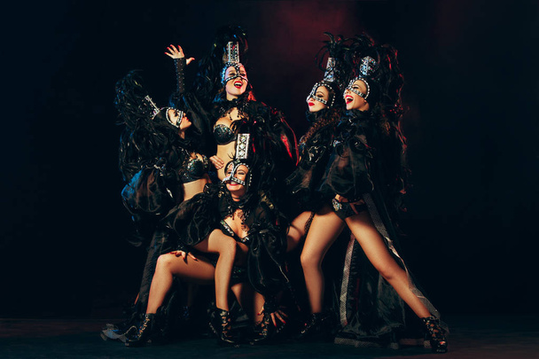 The group of young happy smiling beautiful female dancers with carnival dresses posing on black studio background - 写真・画像