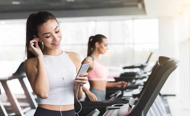 Fitness girl in headphones choosing music on her smartphone - Foto, immagini